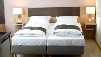 A double bed with white linens and a dark headboard, flanked by bedside tables with lamps, in a modern hotel room.