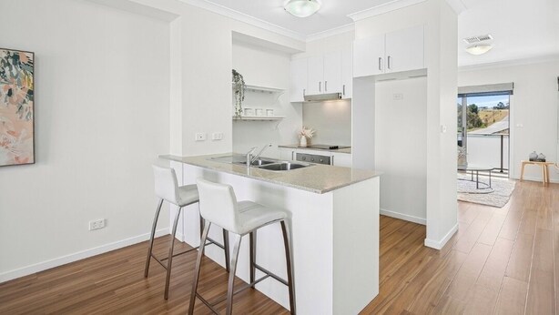 A modern kitchen with white cabinetry, a central island with bar stools, and a view to the dining area. - Modern Townhouse in Wright with Mt Stromlo Views (Wright)