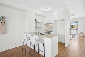 A modern kitchen with white cabinetry, a central island with bar stools, and a view to the dining area.