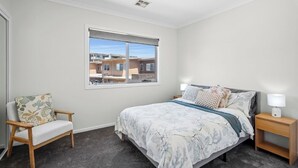 A bedroom with a bed, a chair, a nightstand, and a window with a view of buildings. - Modern Townhouse in Wright with Mt Stromlo Views (Wright)