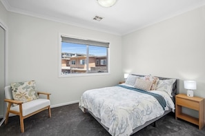 A bedroom with a bed, a chair, a nightstand, and a window with a view of buildings.