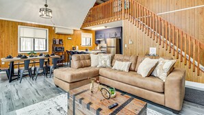 Ein gemütliches Wohnzimmer mit einem großen, beigefarbenen Ecksofa, einer Holztreppe und einer Küche im Hintergrund.