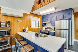 A modern kitchen with wooden paneling, a large island with bar stools, stainless steel appliances, and a window with blinds.