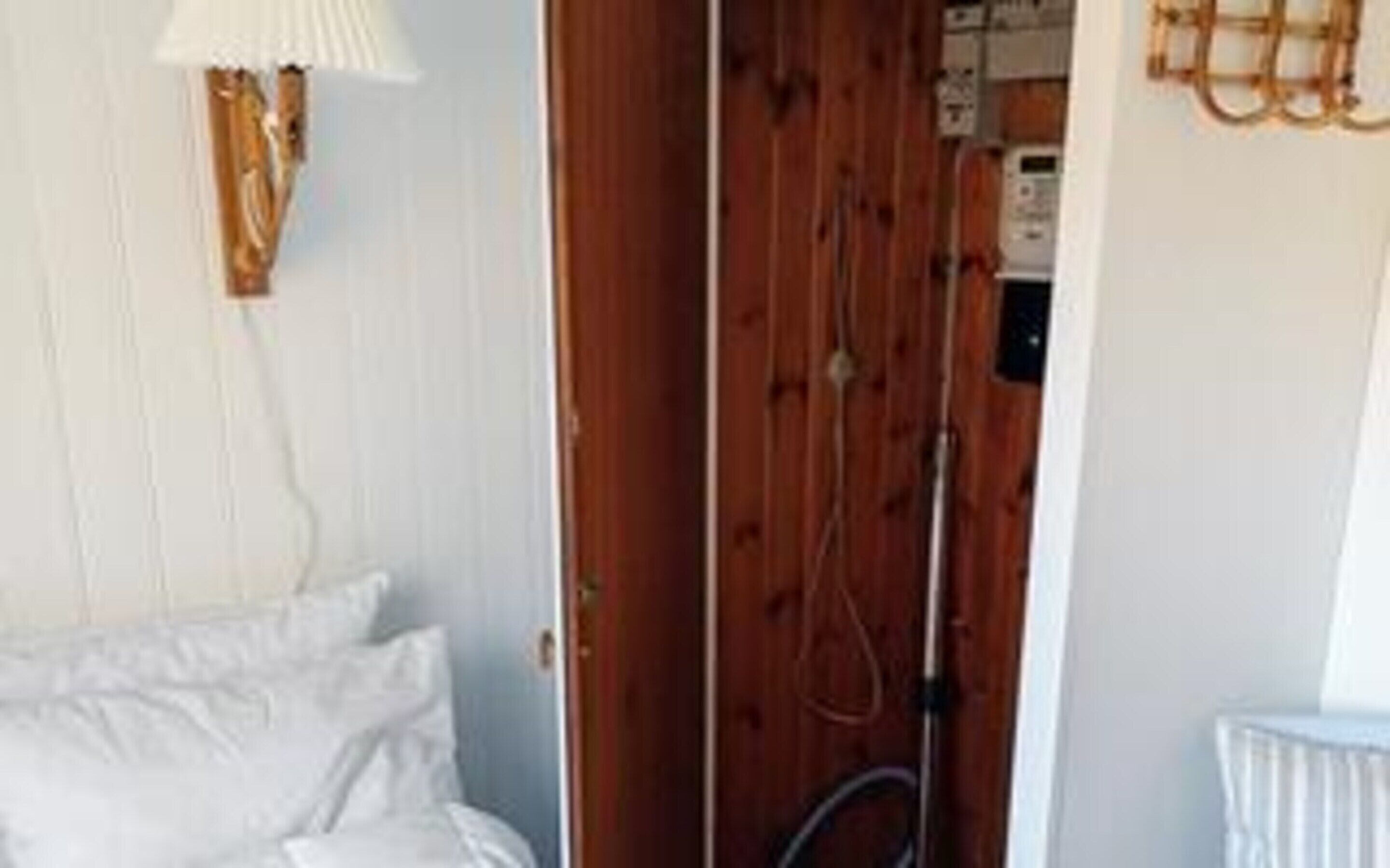 A bedroom with a bed, a wooden door, and a wall-mounted lamp.