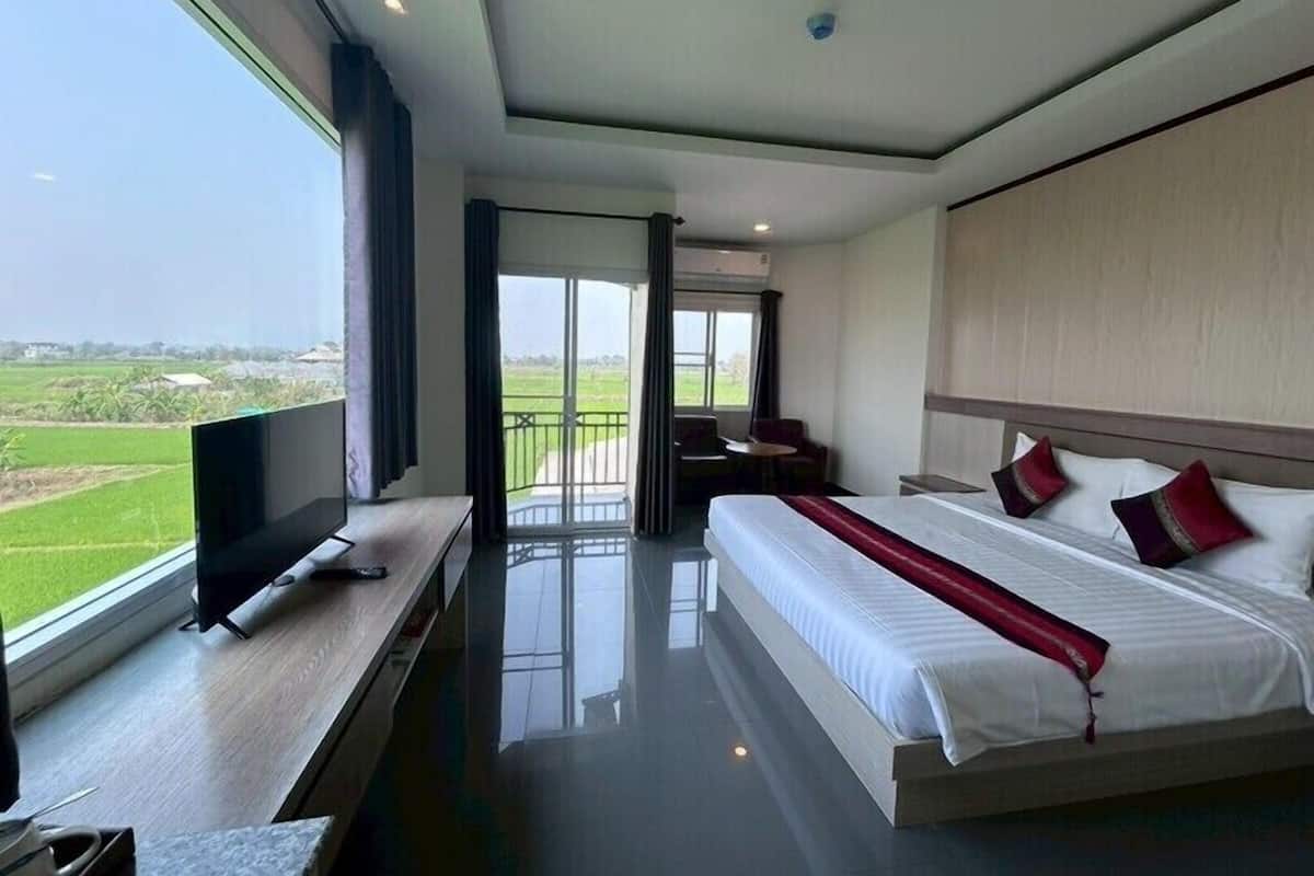 Quarto de hotel com uma cama grande, uma televisão sobre uma mesa de madeira e uma varanda com vista para o campo.
