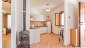 Una cocina moderna con estufa de leña integrada, armarios blancos y piso de baldosas.