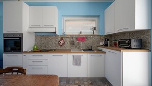 Una cocina con armarios blancos, microondas, tetera y una ventana con persianas.