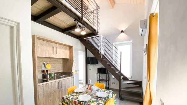 Un coin repas avec une table dressée pour quatre personnes, une cuisine dotée de meubles en bois et un escalier menant à l’étage supérieur.