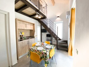 Un comedor con una mesa dispuesta para cuatro, una cocina con armarios de madera y una escalera que conduce a un nivel superior.