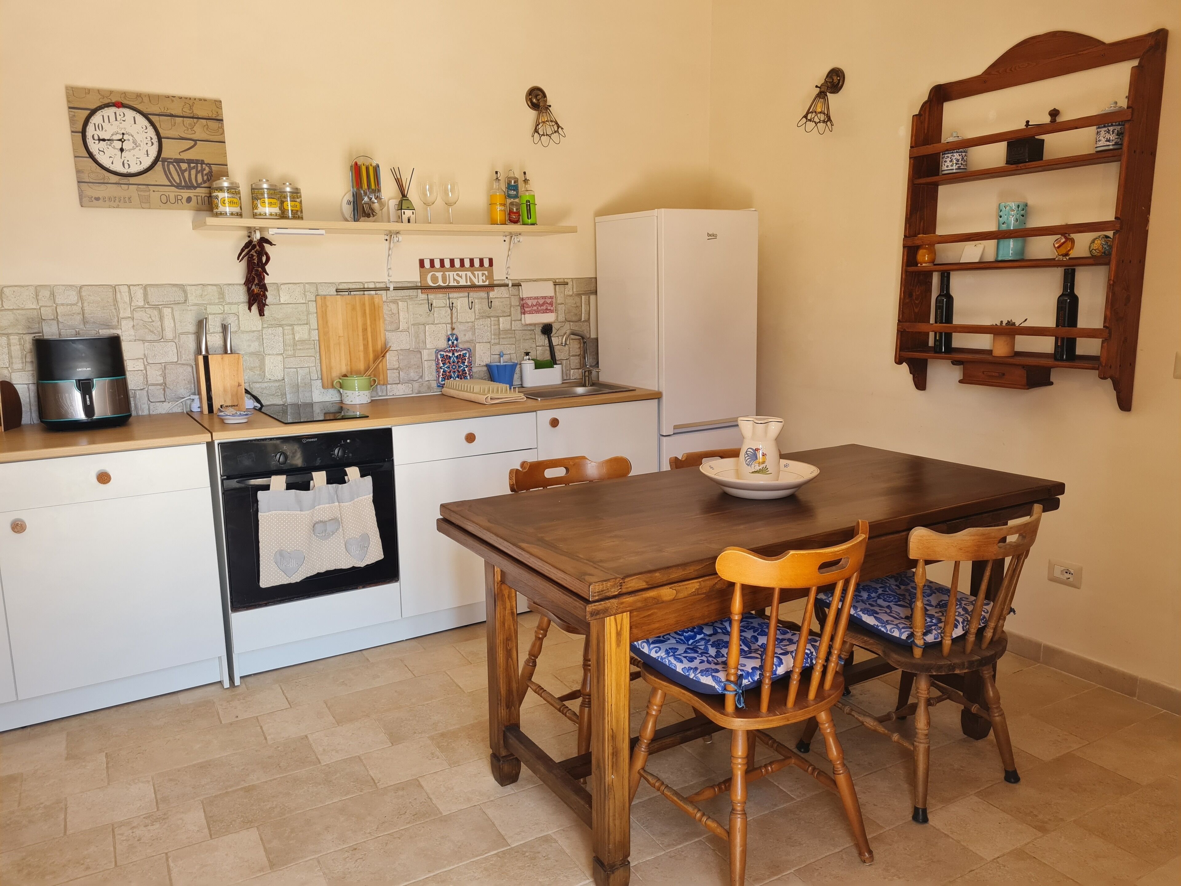 A compact kitchen with a wooden table and chairs, a refrigerator, and various kitchen items on the counter.