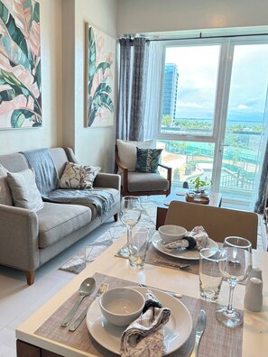 A modern living room with a dining area, large windows with a city view, and tropical-themed artwork. - Pond & Sea View, Mactan Strait (Lapu-Lapu)