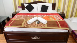 A neatly made bed with a brown headboard, white and black pillows, and a red and beige bedspread. There are two rolled towels and a small bottle on the bed. - ANAYA GUEST HOUSE & RESTAURANT ETAH (Etah)