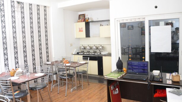 A compact kitchen with a stove, cabinets, and a dining area with chairs and a table. - ANAYA GUEST HOUSE & RESTAURANT ETAH (Etah)
