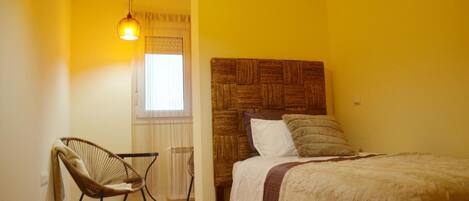 A bedroom with a bed, a chair, a radiator, and a window with curtains.