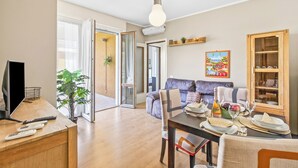 A modern living room with a sofa, dining table, and a TV on a wooden desk. - Casa Mirella Quiet 2BR With View, Balcony and AC (Nebbiuno)