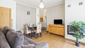 A living room with a gray sofa, dining table, chairs, a TV, wooden cabinets, and a potted plant. - Casa Mirella Quiet 2BR With View, Balcony and AC (Nebbiuno)