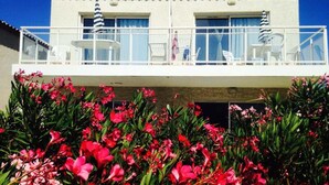 Un edificio de dos pisos con un balcón, barandillas blancas y asientos al aire libre.
