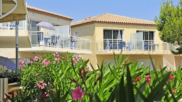 A two-story building with balconies, outdoor seating, and a garden with pink flowers. - Apartment in Gruissan Near Clape Mountain (Gruissan)