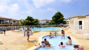 A swimming pool area with multiple pools, surrounded by buildings and a fenced area. - Apartment in Gruissan Near Clape Mountain (Gruissan)
