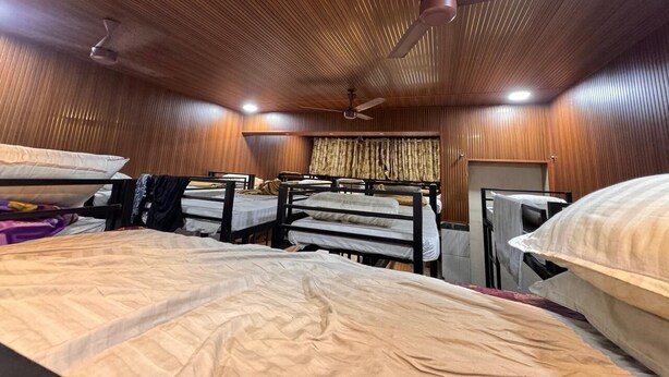 Een kamer met stapelbedden, houten lambrisering, plafondventilatoren en een raam met gordijnen.