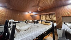 Een kamer met stapelbedden, houten lambrisering, een plafondventilator en een raam met gordijnen.