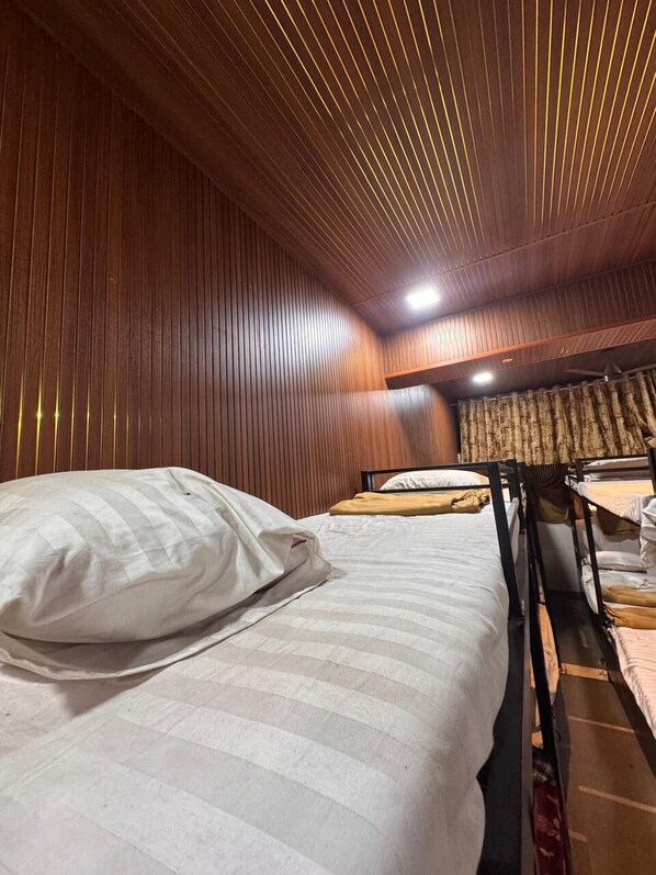 Una habitación con paneles de madera, una cama litera y un ventanal cubierto por una cortina.