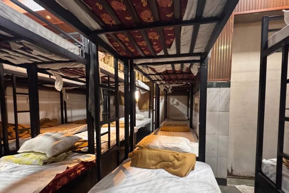 Un couloir étroit, avec des lits superposés de chaque côté, des poutres en bois au plafond et un mur recouvert de carreaux.