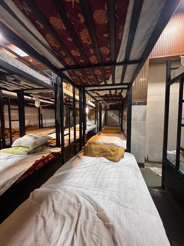 Ein schmaler Korridor mit Etagenbetten an beiden Seiten, Holzbalken an der Decke und einer gefliesten Wand.