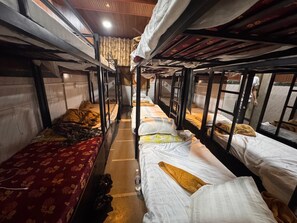 Ein schmaler Korridor mit Etagenbetten an beiden Seiten, Fliesenboden und Deckenventilator.