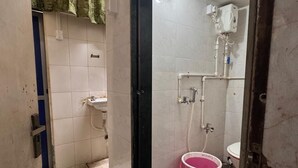 Een kleine badkamer met een douche, wastafel en een roze emmer.