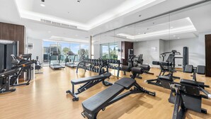 Ett modernt gym med olika typer av träningsutrustning, stora fönster och ett trägolv.