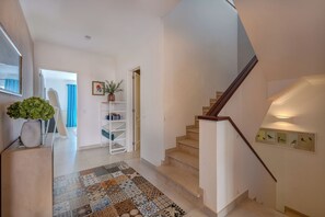 A staircase leading to a landing with a patterned rug, a potted plant, and a white shelving unit. - Stunning beach house, panoramic views across Meia Praia bay (Lagos)