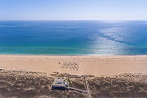 An aerial view of a beach with a clear sky, a sandy shore, and a small building with a dock. - Stunning beach house, panoramic views across Meia Praia bay (Lagos)