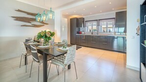 A modern kitchen with dark cabinets, a central island, and a dining area with a table set for four. - Stunning beach house, panoramic views across Meia Praia bay (Lagos)