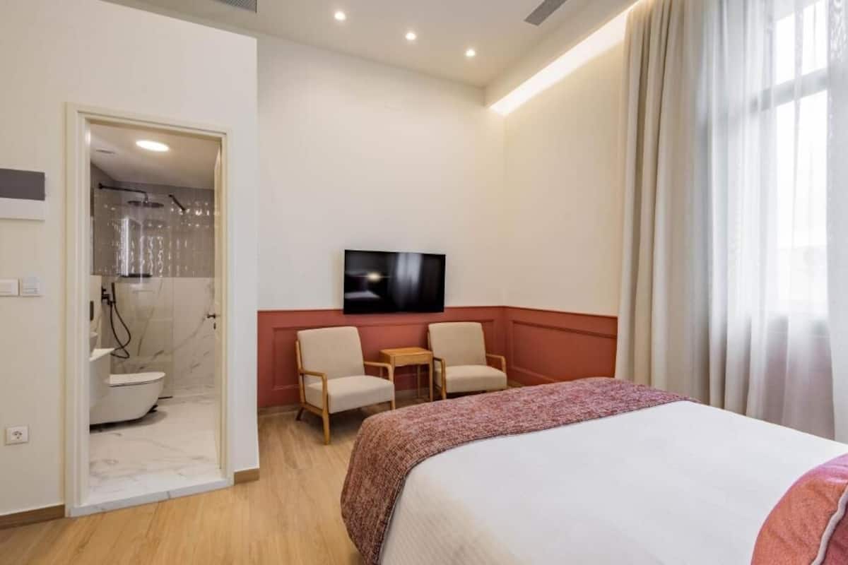 A hotel room with a bed, two chairs, a TV, and a shower area.