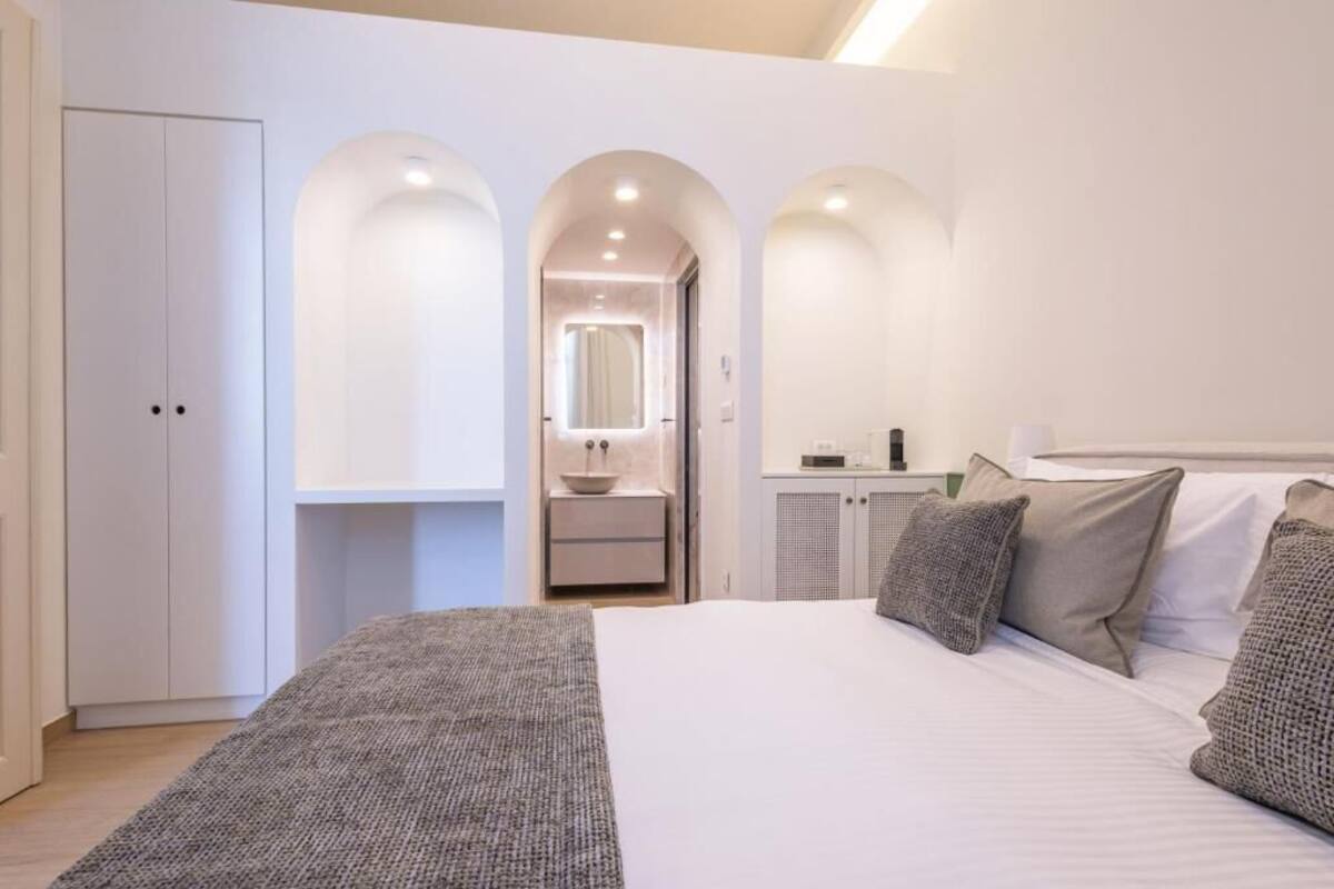 A bedroom with a large bed, a wardrobe, a vanity with a mirror, and a small cabinet.