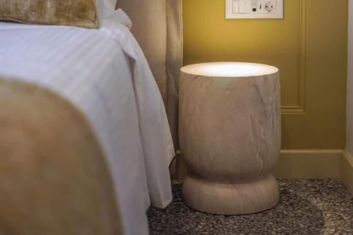 A bedroom with a bed, a bedside lamp, a wall socket, and a door.