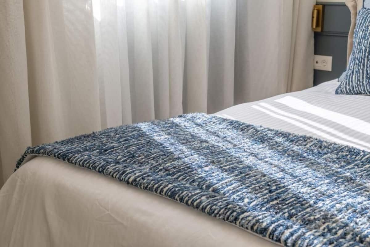 A bed with a striped bedspread and a blue textured blanket.