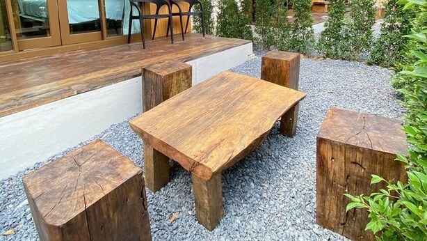 A modern outdoor seating area with wooden tables and chairs, surrounded by gravel and greenery. - Aonang green tree (Krabi)