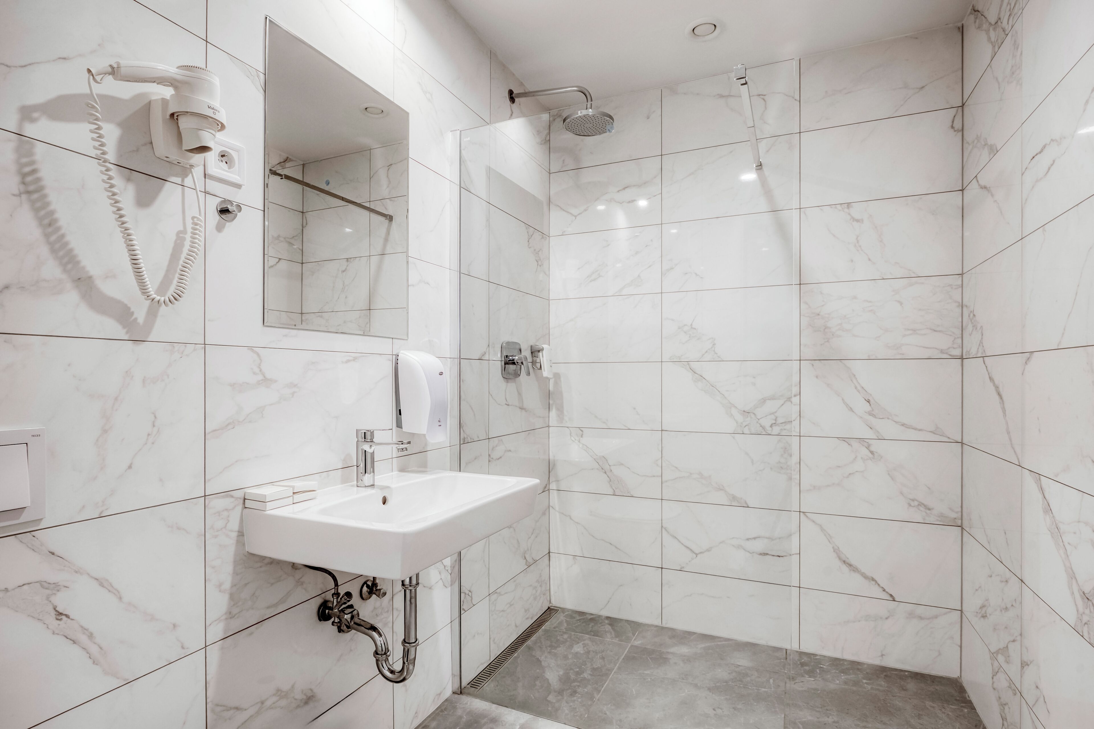 A modern bathroom with a white sink, a hairdryer, a mirror, and a shower.