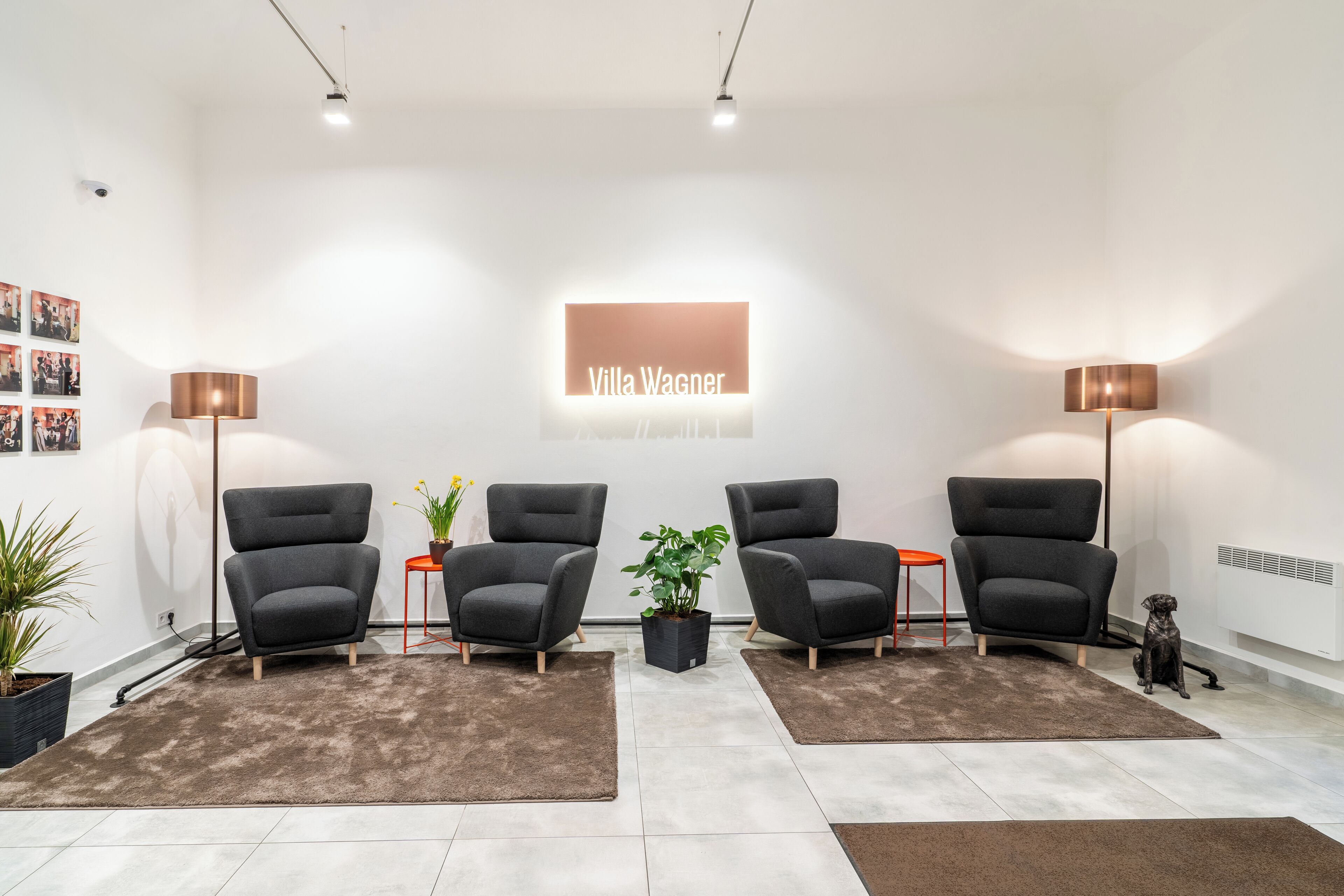 A modern interior with four grey armchairs, a central potted plant, and a sign reading "Villa Wagner".