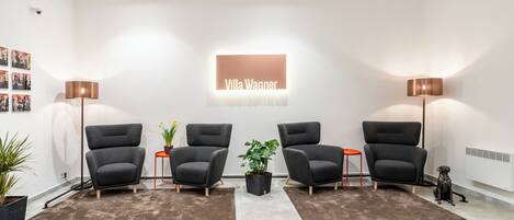 A modern interior with four grey armchairs, a central potted plant, and a sign reading "Villa Wagner".