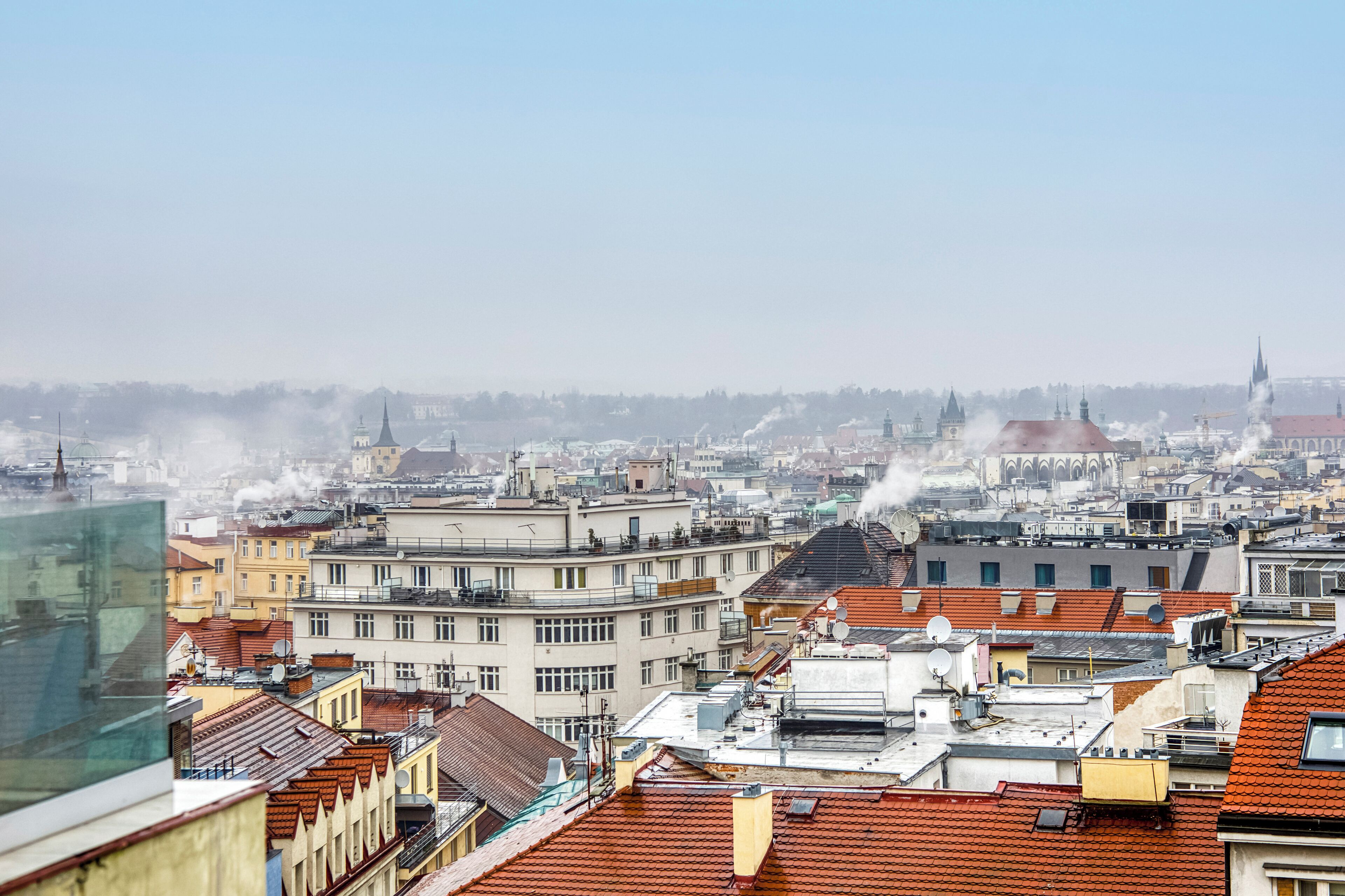 A cityscape with multiple buildings, some with visible rooftops and chimneys emitting smoke.