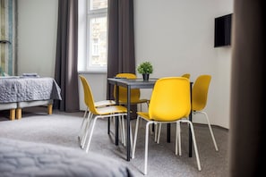 A room with a bed, a table with chairs, a small potted plant, and a window with curtains.