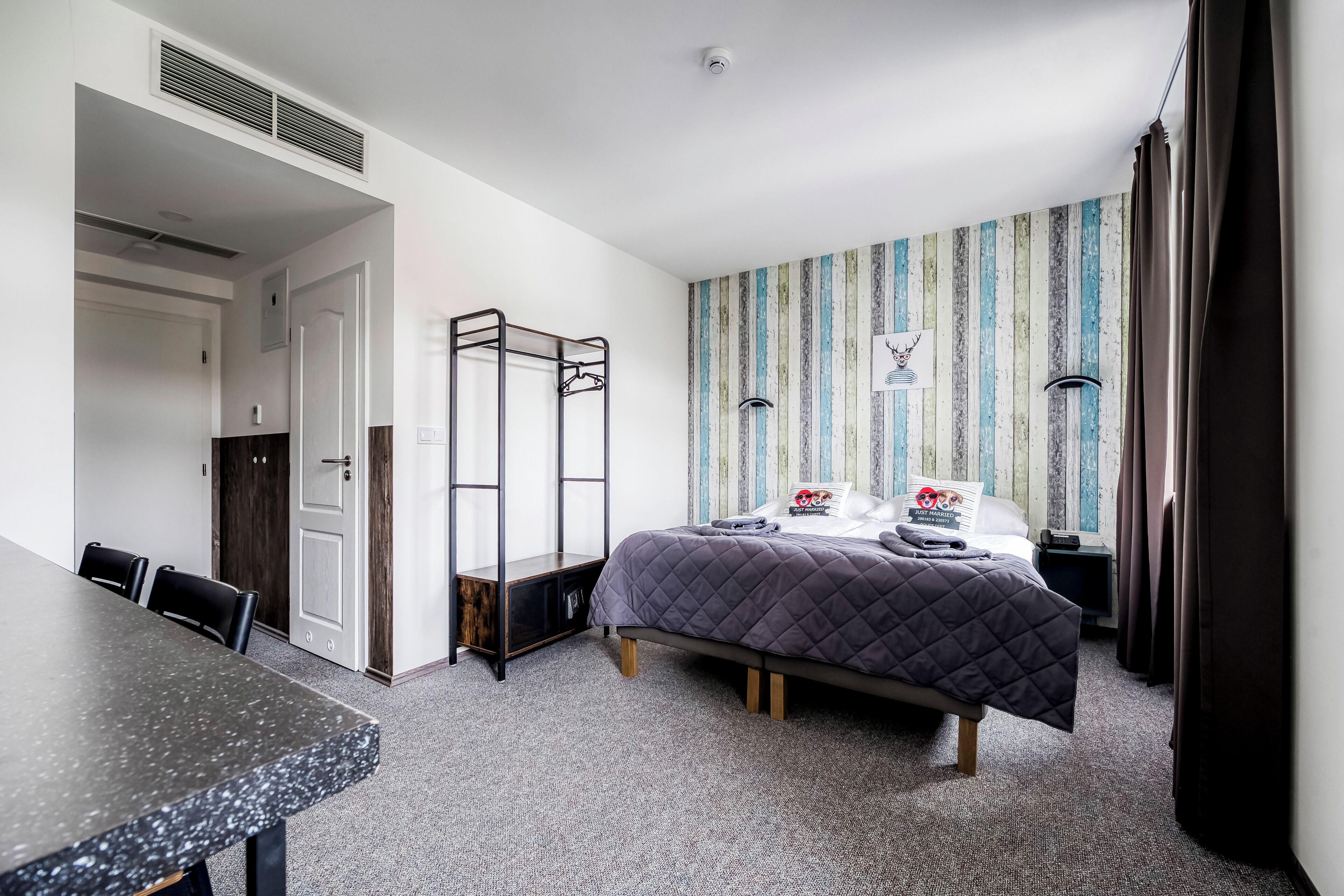A hotel room with a bed, a desk, a chair, a wardrobe, and a striped wall.