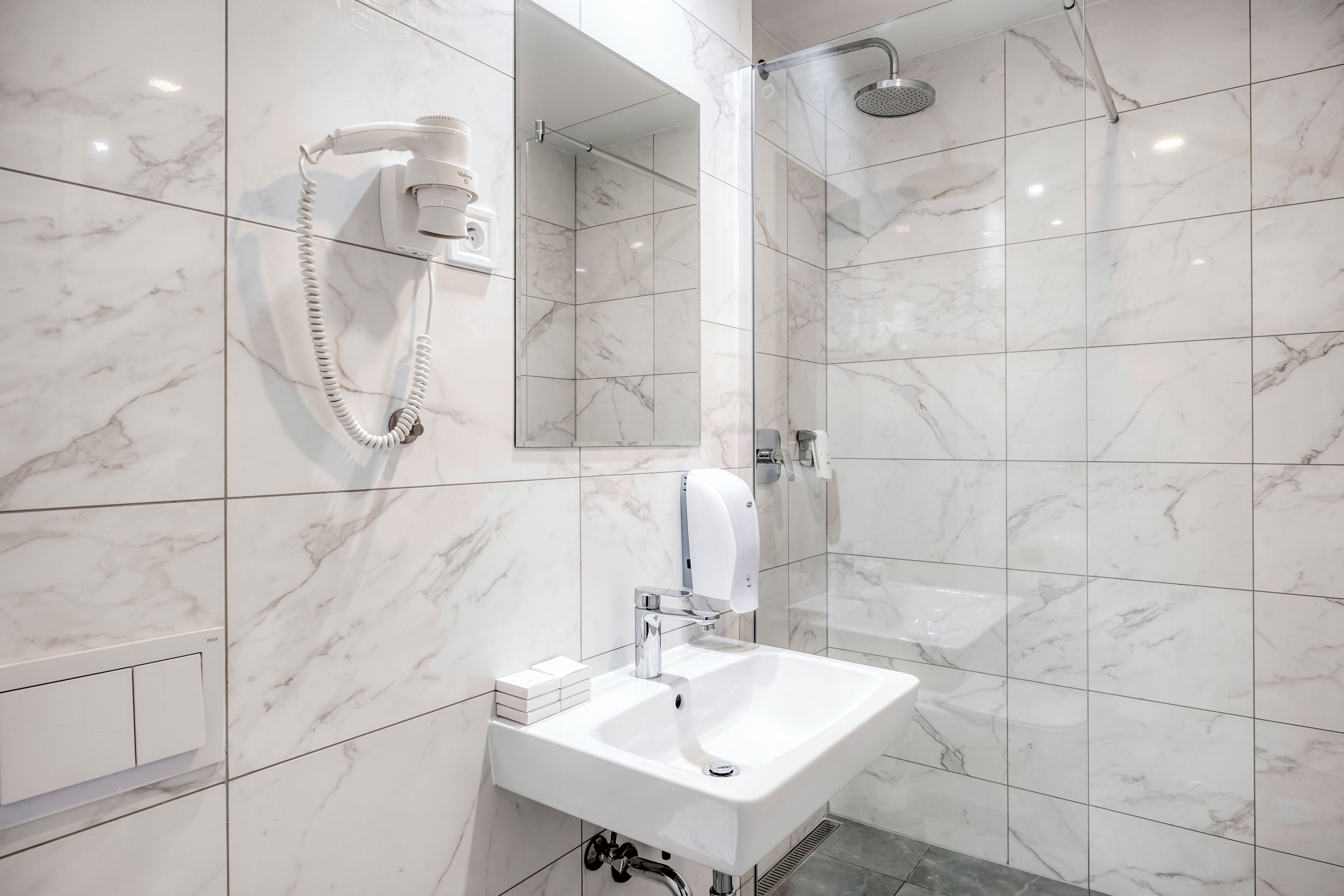 Un baño moderno con pared de azulejos de mármol, lavamanos integrado, cabezal de ducha de mano y mampara de vidrio.