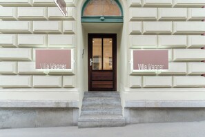 Een gebouwentree met een dubbele deur, een paar stenen treden, en twee borden aan weerszijden van de deur met de tekst 'Villa Wagner'.