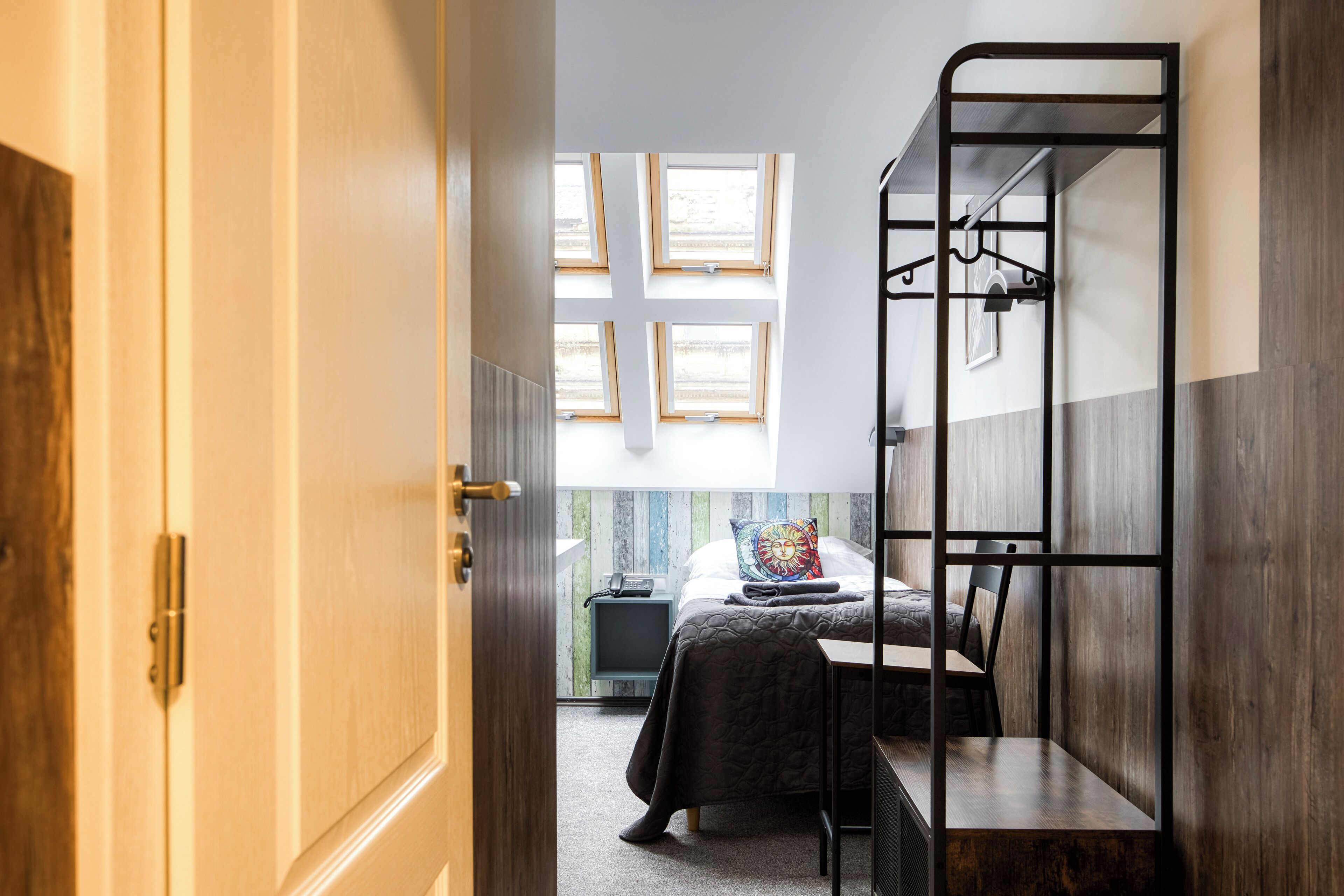 A room with a bunk bed, a desk, a chair, a small bedside table, and a window with multiple panes.