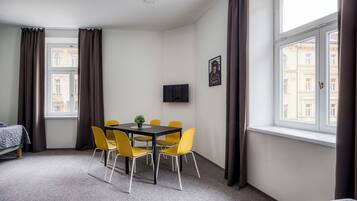 A hotel room with a bed, a dining table with chairs, a TV, and a window with curtains.