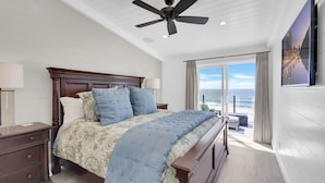 Una camera da letto con un letto grande, una ventola a soffitto, un comodino, una lampada, una finestra vista mare e un quadro appeso al muro.